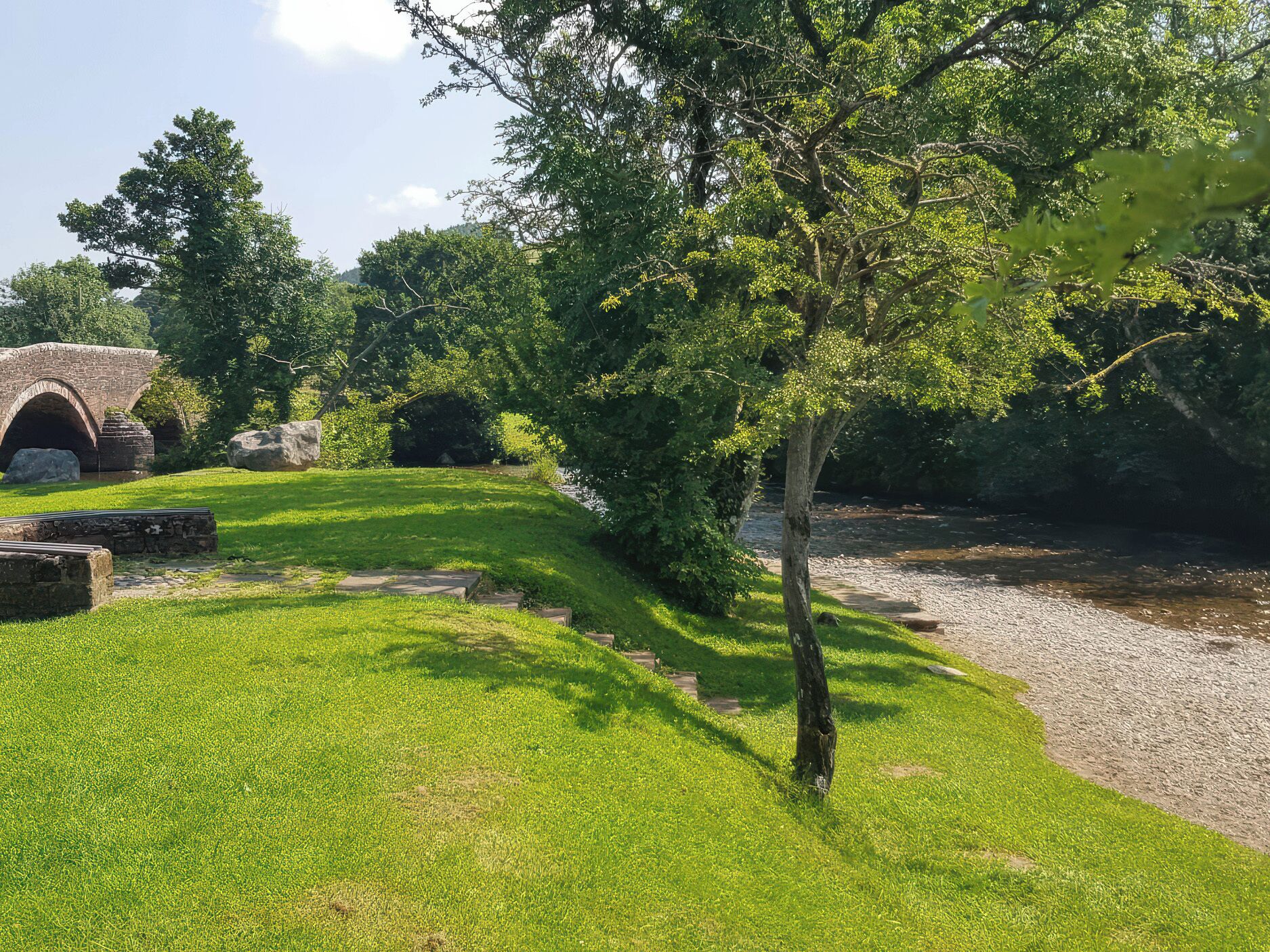 A stone bridge, a grassy area, and a tree.
