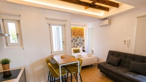 A compact room with a bed, a sofa, a dining table with chairs, and a kitchenette. - Stay Near El Rastro for 4 (Madrid)