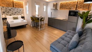 A modern hotel room with a sofa, dining area, kitchen, and a large window. - Stay Near El Rastro for 4 (Madrid)