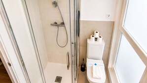 A modern bathroom with a glass shower enclosure, a toilet with a bidet attachment, and a window providing natural light. - Stay Near El Rastro for 4 (Madrid)