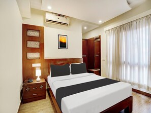 Ein Hotelzimmer mit Bett, Nachttisch, Lampe, Klimaanlage, Kunstwerk und Kleiderschrank.
