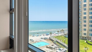 A view of a beach with a swimming pool, palm trees, and a building in the background. - 🌴Amazing Ocean Views | Beachfront Pool | Oceanside Inn 605🌴 (Daytona Beach)
