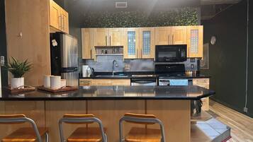 Una cucina moderna con mobili in legno, un piano di lavoro nero, elettrodomestici in acciaio inossidabile e tre sgabelli da bar.
