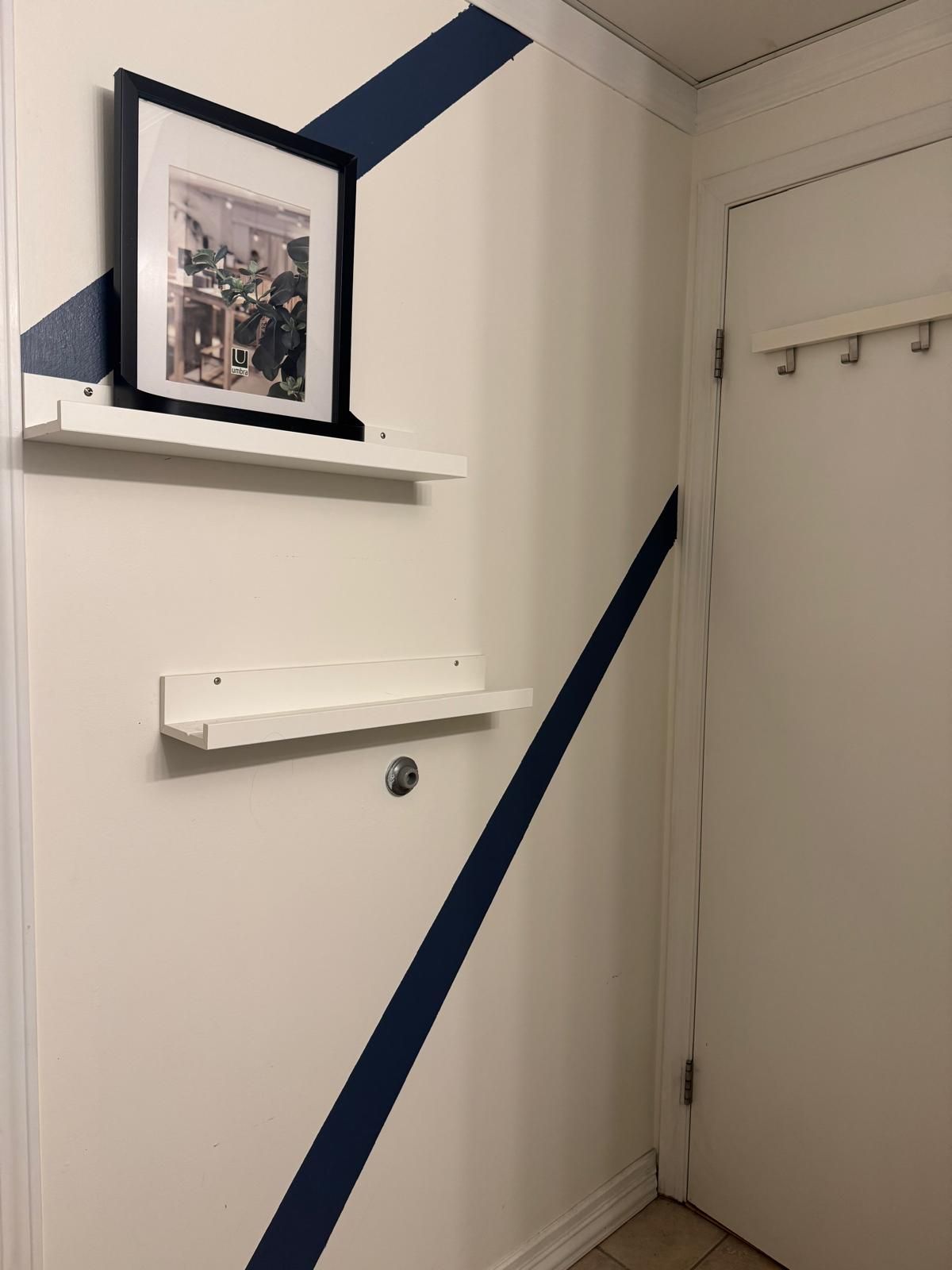 Um corredor com uma porta branca, um quadro em uma prateleira branca e uma faixa azul na parede.