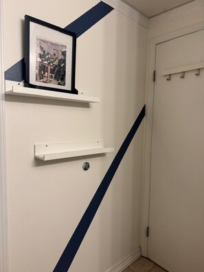 Un pasillo con una puerta blanca, un cuadro en un estante blanco y una franja azul en la pared.