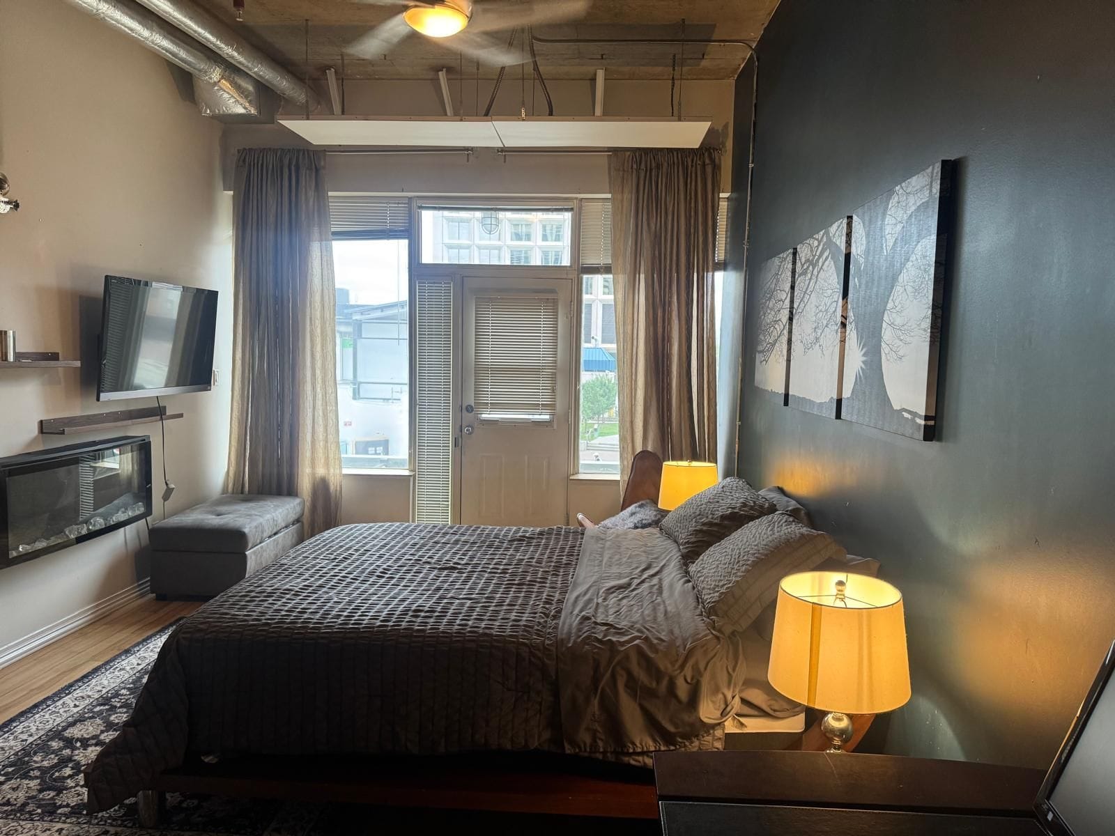 Habitación de hotel con cama, televisión, escritorio con lámpara y vista al exterior a través de una ventana.