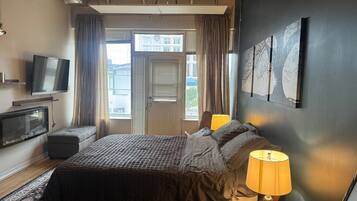 Habitación de hotel con cama, televisión, escritorio con lámpara y vista al exterior a través de una ventana.