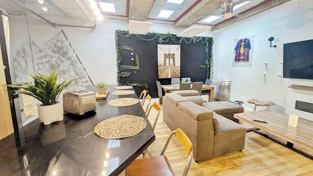 A modern interior with a long table, chairs, sofas, and a black accent wall with greenery.