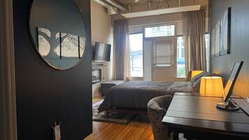 A bedroom with a bed, a desk, a chair, a television, and a window with curtains.
