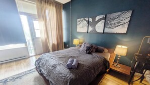 A bedroom with a large bed, two bedside lamps, a view of the outdoors through a window, and a wall with three framed pictures.