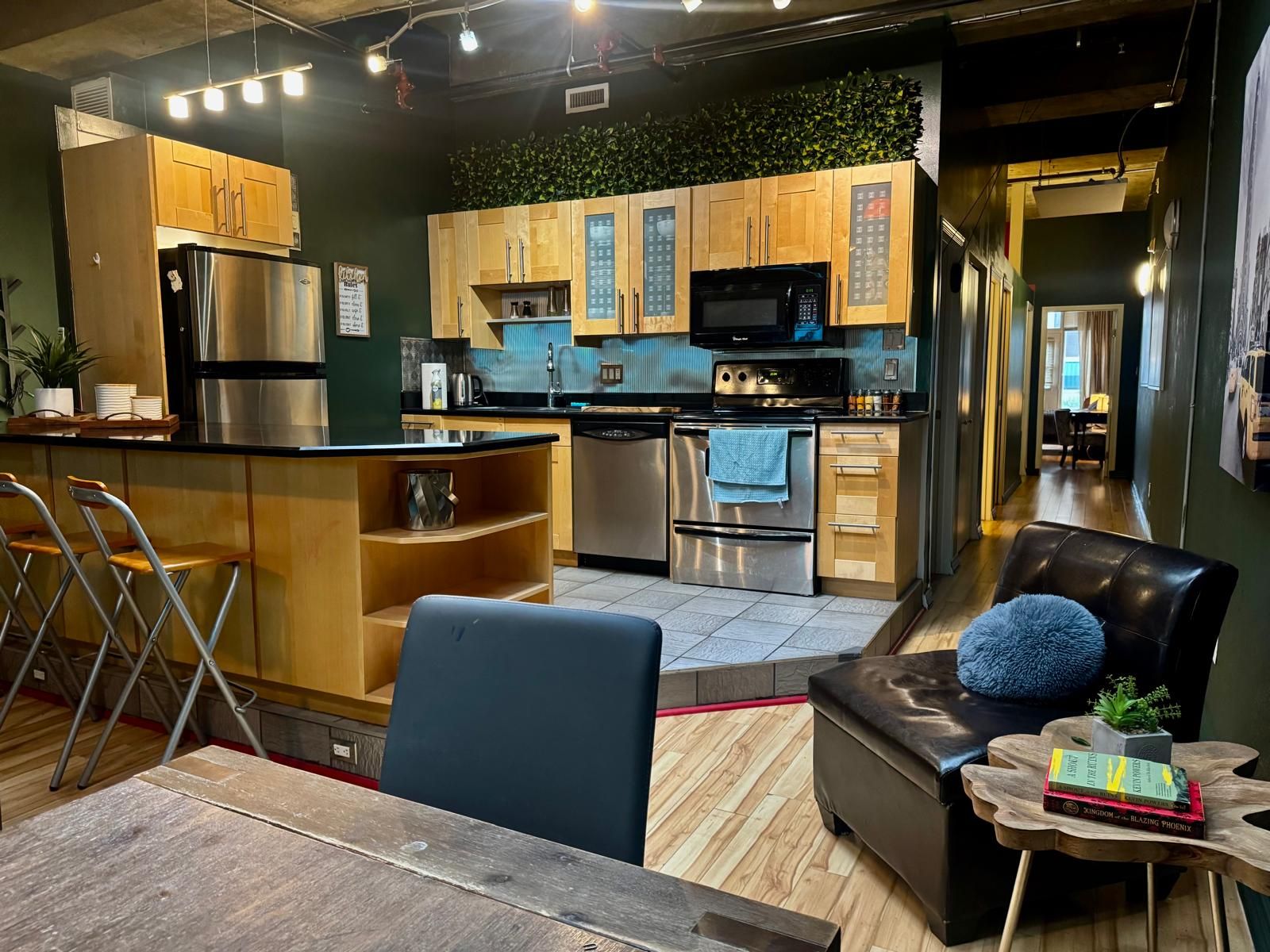 A modern kitchen with wooden cabinets, stainless steel appliances, and a dining area with a leather couch and a small side table.