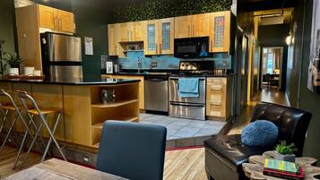 A modern kitchen with wooden cabinets, stainless steel appliances, and a dining area with a leather couch and a small side table.
