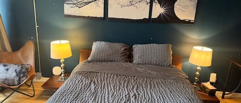 A bedroom with a bed, two bedside lamps, a chair, and a wall-mounted painting.