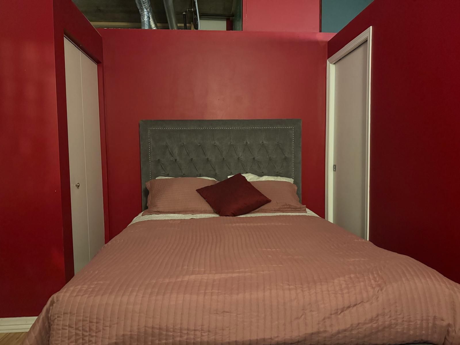 Un dormitorio con una cama, cabecera y paredes rojas.