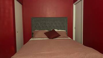 Un dormitorio con una cama, cabecera y paredes rojas.