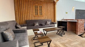 A cozy outdoor seating area with a wooden wall, a sofa, a table, and a grill.
