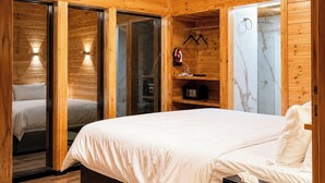 A wooden cabin bedroom with a bed, a bedside table, a hanging light fixture, and a shower area.