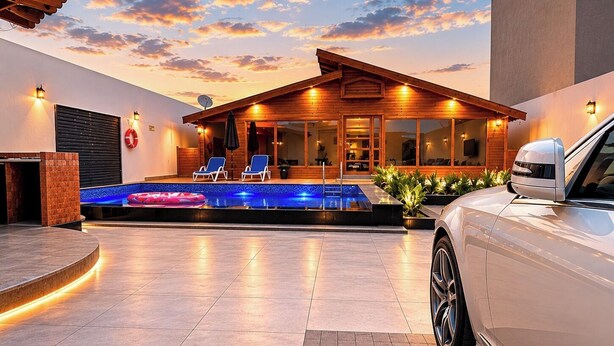 A modern house with a swimming pool, lounge chairs, and a car parked in front.