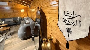 A cozy cabin interior with wooden walls, a grey sofa, a small table, and a decorative wall hanging.