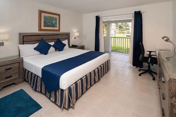 Habitación de hotel con cama, escritorio, silla, cómoda, mesita de noche y vistas al exterior.