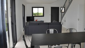 A modern living room with a dark sofa, a TV, and a dining area with a table and chairs. - Villa Pradel – Holiday Home Guérande La Baule, 4 Bedrooms, 7 Guests (Guérande)