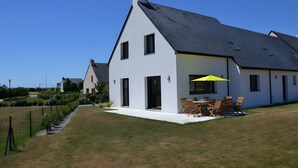 A modern two-story house with a sloped roof, a patio with outdoor furniture, and a clear blue sky. - Villa Pradel – Holiday Home Guérande La Baule, 4 Bedrooms, 7 Guests (Guérande)