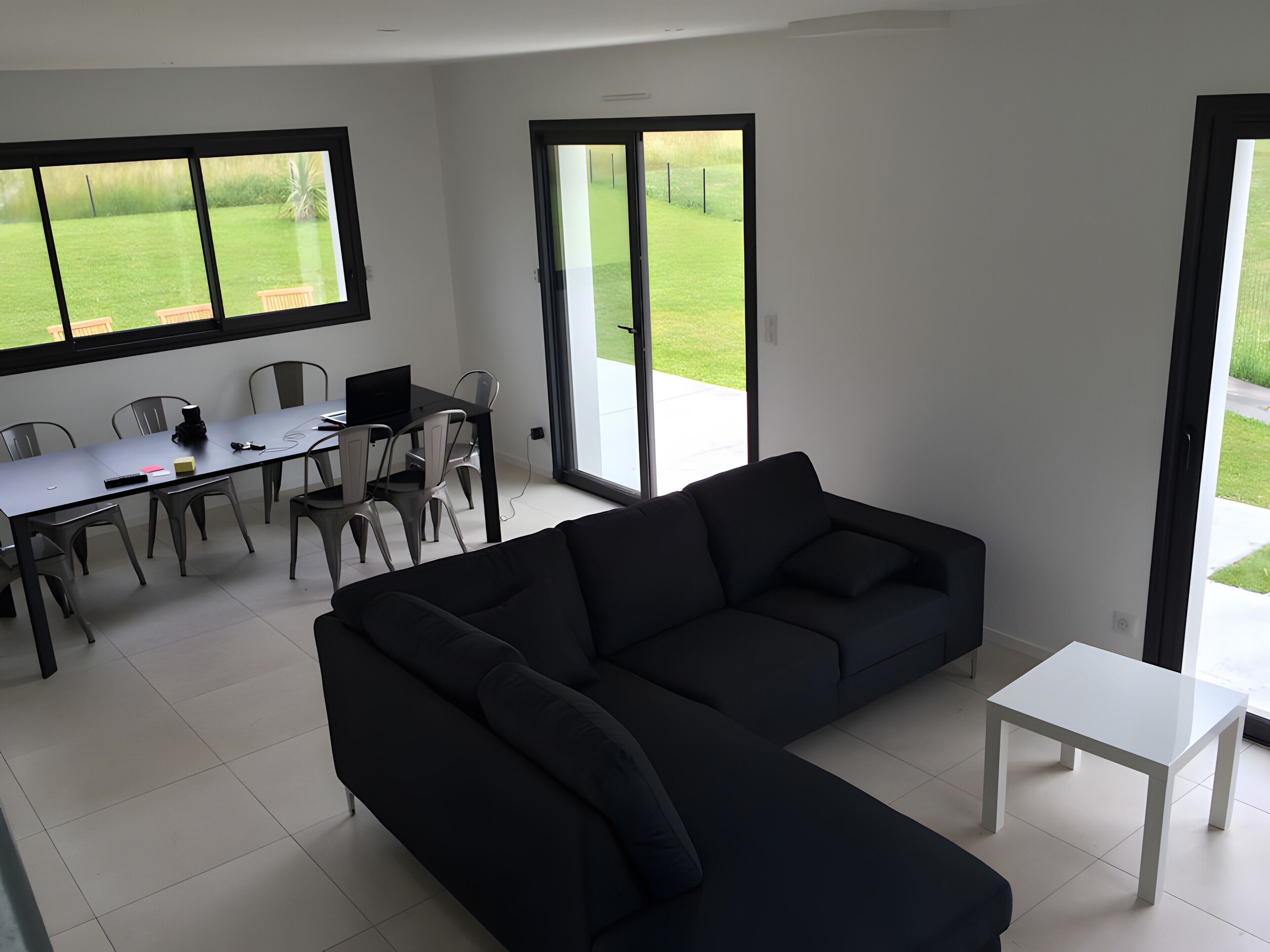 A modern living room with a black sofa, a white coffee table, and a dining area with chairs and a table.