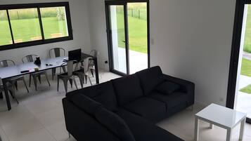 A modern living room with a black sofa, a white coffee table, and a dining area with chairs and a table.