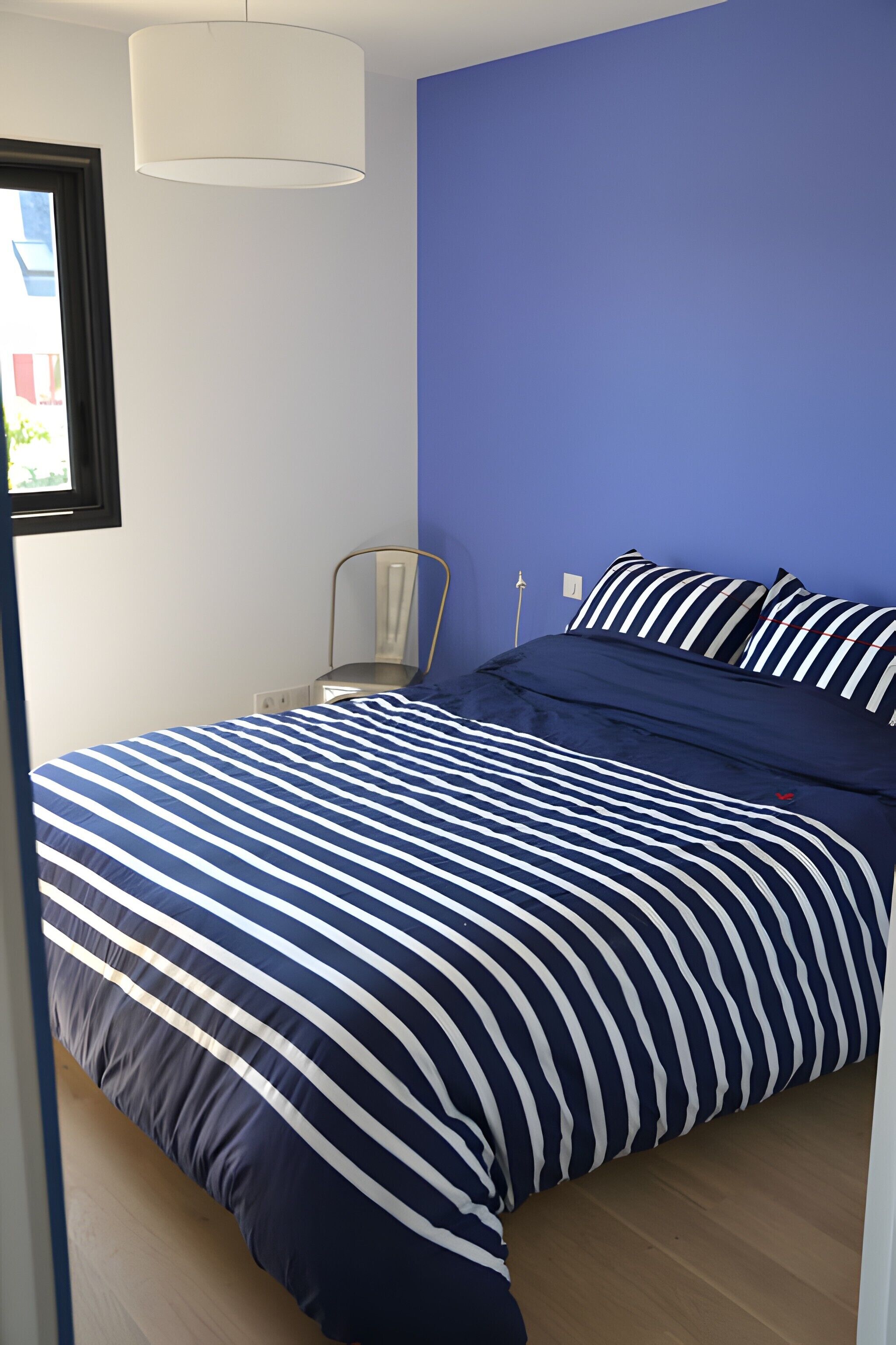 Une chambre à coucher avec un lit, une chaise, une fenêtre et une lampe.