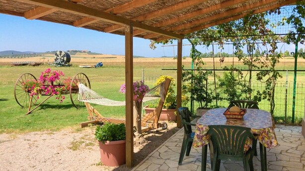 Una veranda riparata con tavolo e sedie, un'amaca e vasi di piante.