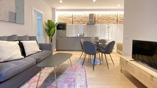 A modern living room with a sofa, coffee table, TV, and a dining area with chairs. - Stay in Madrid for 5 Guests (Madrid)