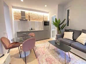 Ein modernes Wohnzimmer mit einem grauen Sofa, zwei rosafarbenen Sesseln, einem Glastisch und einem gemusterten Teppich.