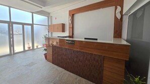 A reception desk with a 'RECEPTION' sign, large windows, and a potted plant. - Classic Pine Villa (Lucknow)