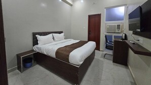 A bedroom with a bed, a desk, a chair, a TV, and a door. - Classic Pine Villa (Lucknow)