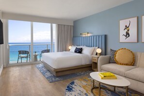 Ein Hotelzimmer mit einem großen Bett, einer Couch, einem kleinen Tisch, einem Sessel und Blick auf den Ozean.