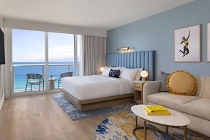 Ein Hotelzimmer mit einem großen Bett, einer Couch, einem kleinen Tisch, einem Sessel und Blick auf den Ozean.