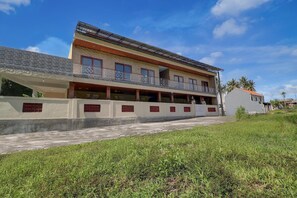 A multi-story building with a balcony, a covered walkway, and a grassy area in front. - Elegant Deluxe DBL Retreat Near Mangusada Hospital (Mengwi)