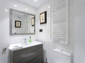A modern bathroom with a white sink, a large mirror, framed pictures, a towel rack, and a toilet. - 6-guest Haven Near Golden Mile (Madrid)