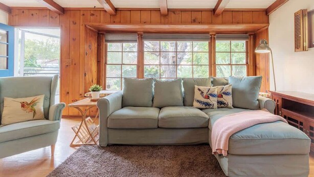 A cozy living room with a sectional sofa, a small table with a plant, and a window with blinds. - 109 GATED Urban LA cottage (Los Angeles)