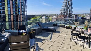 Une terrasse sur le toit avec des sièges extérieurs, une vue sur le paysage urbain et un grand immeuble en arrière-plan.
