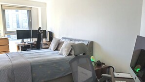Une chambre à coucher avec un lit, un bureau, une chaise, un ordinateur et une fenêtre.