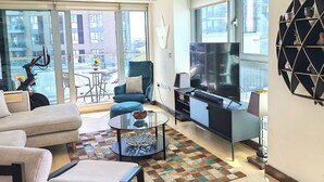 Un salon moderne avec un canapé, un fauteuil et une table basse, un téléviseur et un balcon où se trouve un scooter.