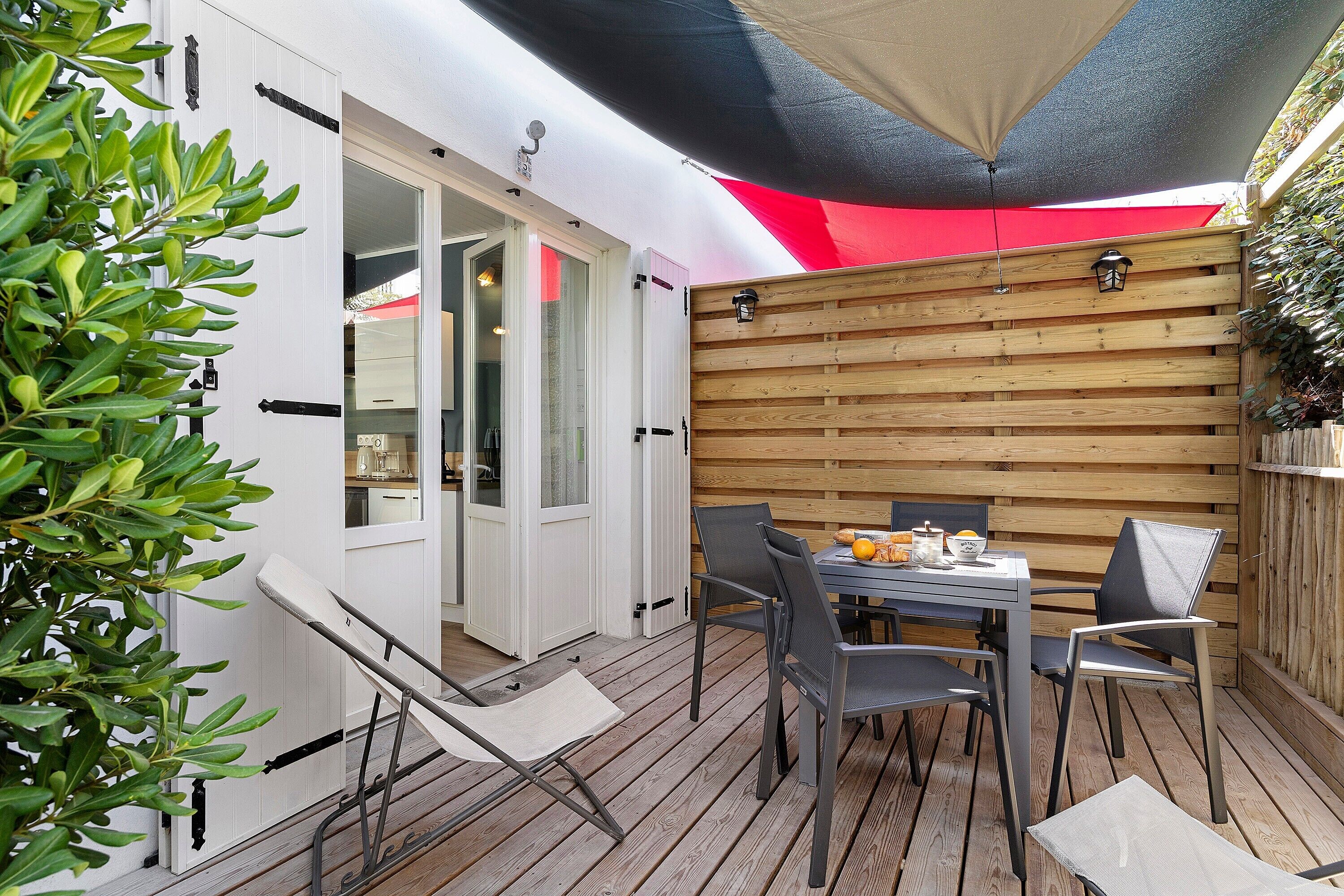 Eine Terrasse mit Tisch und Stühlen, ein Holzzaun und eine Tür, die zu einem Raum führt.