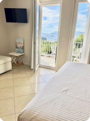 A bedroom with a bed, a TV, a small table with a painting, and a balcony with a view. - Stunning Sunset View Apartment for - Couples &Friends (Cavtat)