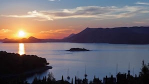 Ein Sonnenuntergang über einem stillen See mit Booten, einer kleinen Insel und fernen Bergen.