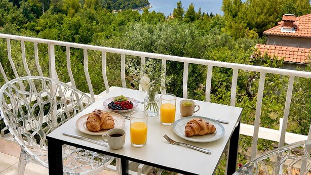 Ein Balkon mit gedecktem Tisch für das Frühstück, mit Blick auf eine schöne Landschaft aus Bäumen und einem Gewässer.