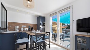 A modern kitchen with a dining area, large sliding glass doors to an outdoor patio, and a flat-screen TV mounted on the wall. - Holiday Home 'L'oeillet Bleu' with Private Terrace, Wi-Fi and Air Conditioning (Saint-Jean-de-Monts)