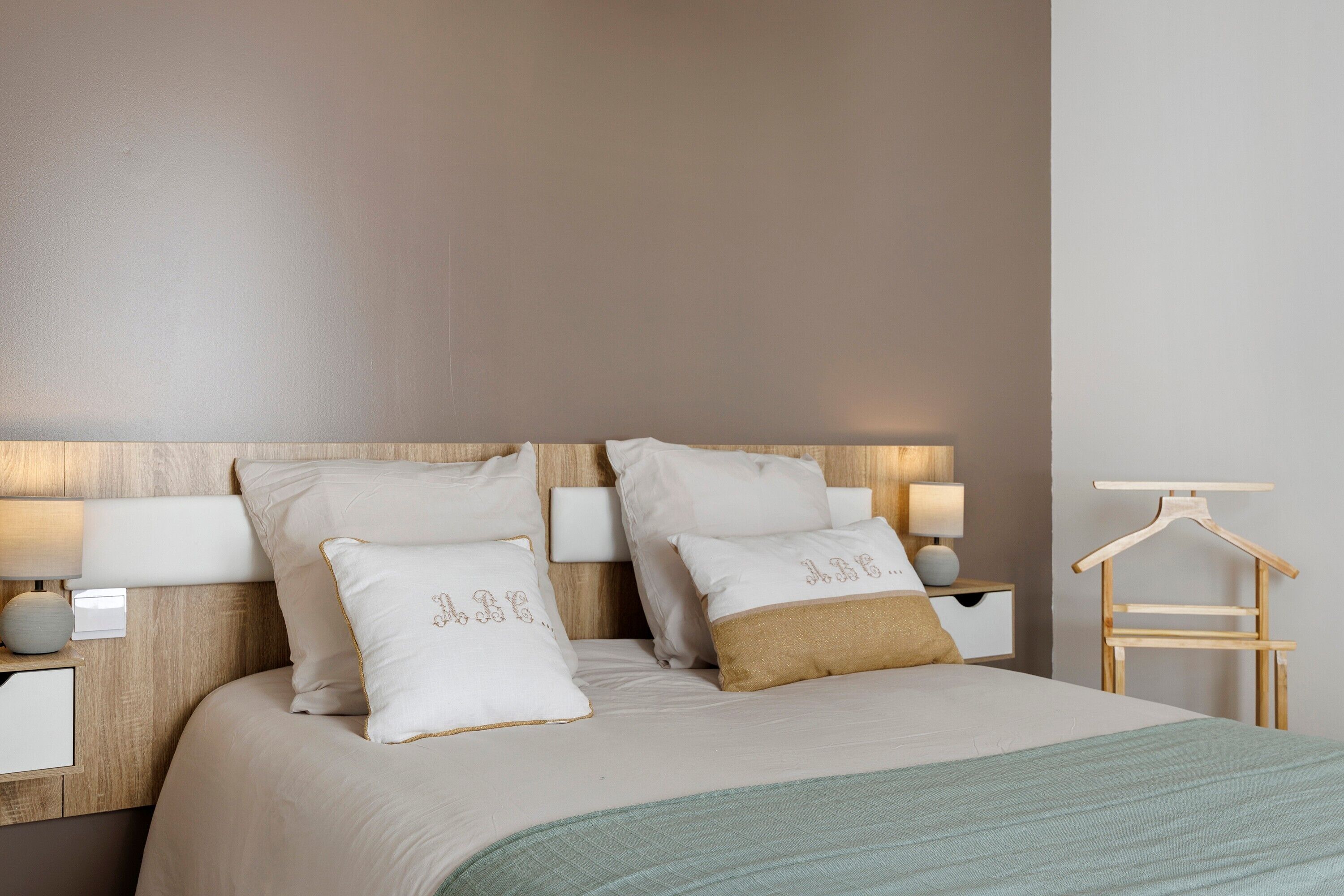 Un lit bien fait, avec des oreillers, une table de chevet avec une lampe et un porte-manteau en bois fixé au mur.