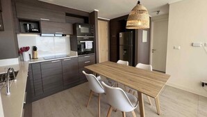 A modern kitchen with dark cabinetry, a wooden dining table, and white chairs. - Vina del Mar 2BR sea views & balcony (Viña del Mar)
