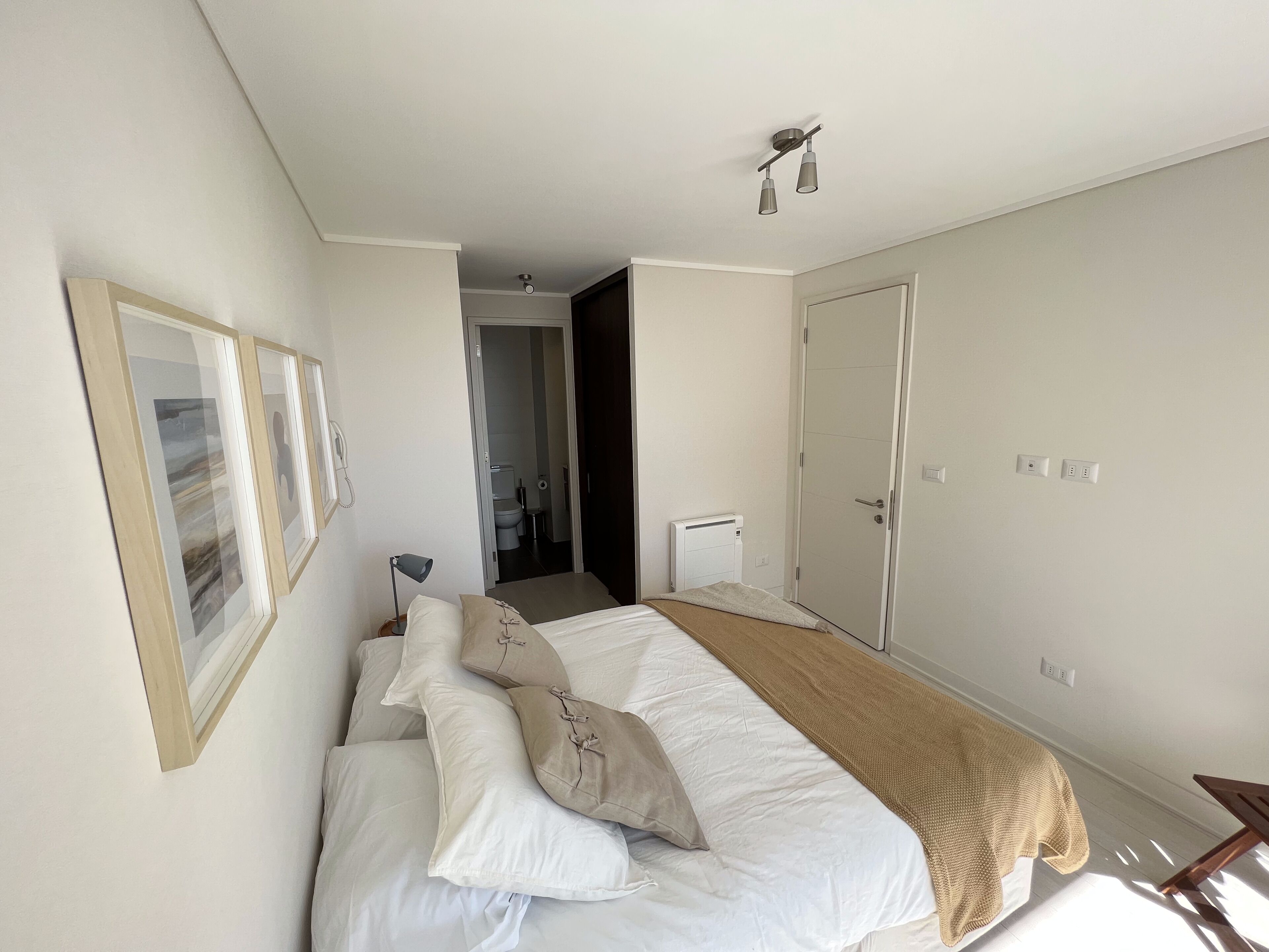 Un dormitorio con cama, mesita de noche, lámpara, puerta y teléfono en la pared.